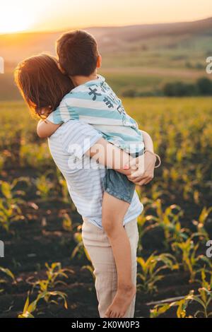 Mère et fils s'embrassant avec affection pendant qu'ils regardent le coucher du soleil du champ ensemble. Mère nature. Nature estivale. Bonne famille Banque D'Images