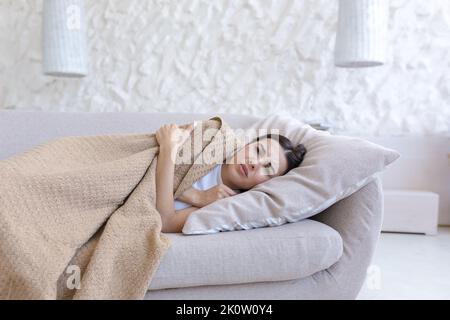 Jeune femme malade couché sur un oreiller sur le canapé à la maison, recouverte d'une couverture brune. Il se sent mal, froid, gelé, au repos Banque D'Images