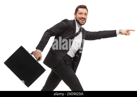 Homme d'affaires dans un costume noir courant avec une serviette et pointant vers l'avant isolé sur fond blanc Banque D'Images