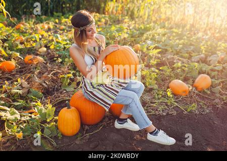 Récolte de citrouilles. Une jeune femme paysanne cueille des citrouilles d'automne à la ferme, assise sur une pile de légumes et ayant du repos. Agriculture. Banque D'Images