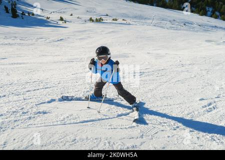 un petit skieur débutant sur une piste de ski dans une position inversée drôle et souriant derrière les lunettes de vue de la caméra, enfant ayant l'apprentissage amusant à Banque D'Images