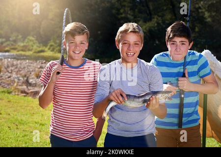 Fiers de leur prise. Portrait de trois jeunes garçons montrant un poisson qu'ils ont attrapé. Banque D'Images