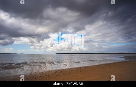 Des nuages de pluie menaçants se forment au-dessus du détroit des Grands Sandy, sur la côte du Fraser, à Poona, dans le Queensland. Des méplats de boue apparaissent à mesure que la marée s'écoule. Banque D'Images