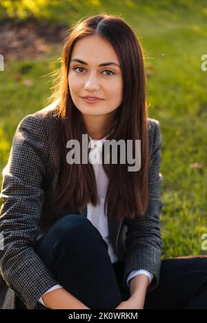 Portrait d'une belle femme d'affaires en veste regardant l'appareil photo, prenant une pause de travail se détendant sur la pelouse verte dans le parc de la ville. Belle fille attrayante Banque D'Images