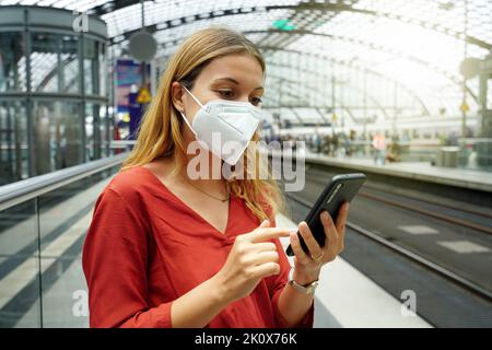 Gros plan d'une femme avec masque facial de protection utilisant un smartphone à la gare de Berlin au coucher du soleil, en Allemagne Banque D'Images