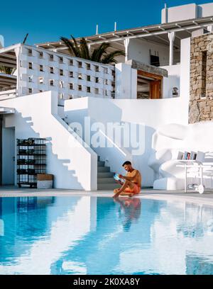 jeunes hommes en short de natation lisant un livre près de la piscine. Bronzage blanc hommes lisant un livre au bord de la piscine Banque D'Images