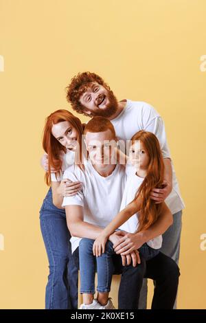 Famille amicale, tête rouge jeunes hommes, femme et enfant portant des vêtements décontractés passer du temps ensemble à la séance photo en studio. Banque D'Images