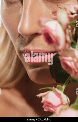 Lèvres tendres. Gros plan d'une belle jeune femme avec fleur isolée sur fond blanc. Concept de cosmétiques, de beauté naturelle et de cosmétologie esthétique Banque D'Images