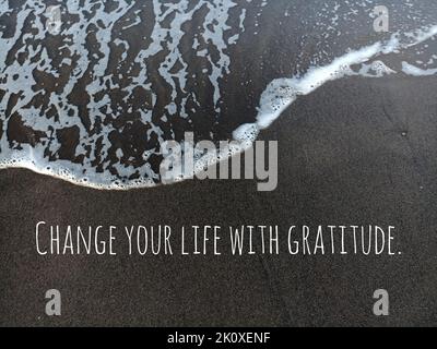 Citation motivante positive - changez votre vie avec gratitude. Sur fond naturel de mousse ondulée sur la plage de sable noir. Soyez reconnaissant. Banque D'Images