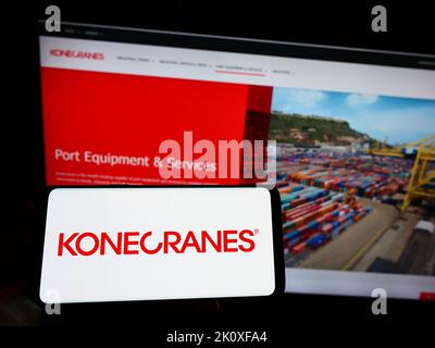 Personne tenant un téléphone portable avec le logo de la société finlandaise de grue Konecranes Oyj sur l'écran en face de la page web d'affaires. Mise au point sur l'affichage du téléphone. Banque D'Images