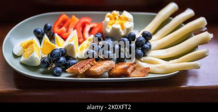 Petite collation saine (petit déjeuner ou dîner) sur l'assiette. Œuf dur en tranches, raisin foncé de vin, fromage, poivron rouge et pain rôti en tranches sur l'assiette de la patte Banque D'Images