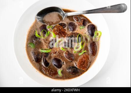 Soupe de haricots géants avec tomates séchées dans une assiette avec cuillère sur fond blanc, gros plan. Banque D'Images