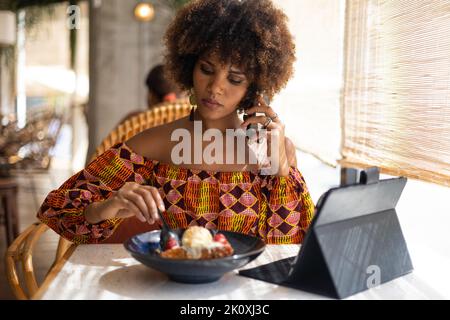 Portrait d'une femme africaine mangeant un dessert tout en parlant au téléphone portable Banque D'Images