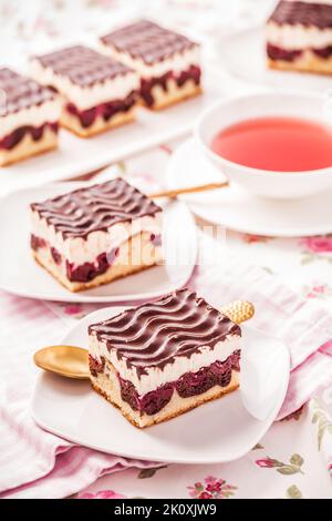 Gâteau allemand Donauwelle (Danube Waves) - gâteau éponge à la vanille et au chocolat avec cerises aigres, crème au beurre à la vanille et glaçage au chocolat avec une tasse de thé Banque D'Images