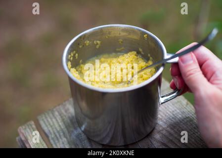 Main tenant le porridge juste cuit avec les légumes dans les ustensiles en métal. Nourriture pour la randonnée, la pêche, la chasse. Copier l'espace Banque D'Images