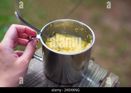 Main tenant le porridge juste cuit avec les légumes dans les ustensiles en métal. Nourriture pour la randonnée, la pêche, la chasse. Copier l'espace Banque D'Images