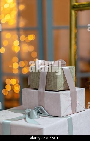 Gros plan sur des boîtes-cadeaux enveloppées de façon fébrile, sur un fond de Noël de lumières étincelantes, un fond magique du nouvel an. Flou artistique, flou sélectif doux Banque D'Images