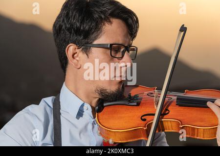 Gros plan portrait d'un homme jouant un violon pour l'écouter au coucher du soleil Banque D'Images