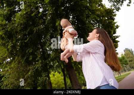 Photo d'adorable maman petite fille vêtements décontractés jouant les bras montant marchant à l'extérieur du jardin Banque D'Images