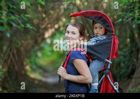 La mère avec un enfant en bas âge dans un sac à dos est en randonnée dans la forêt Banque D'Images