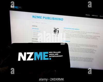 Personne tenant un smartphone avec le logo de la société New Zealand Media and Entertainment (NZME) à l'écran devant le site Web. Mise au point sur l'affichage du téléphone. Banque D'Images