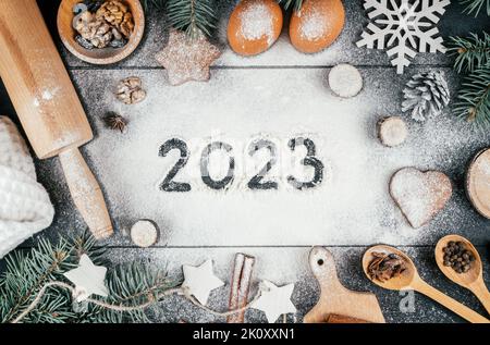 Numéros 2023 inscrits sur la farine saupoudrée sur une table noire avec des branches d'arbre de Noël, des accessoires de cuisson et des ingrédients. Joyeux Noël et heureux Banque D'Images