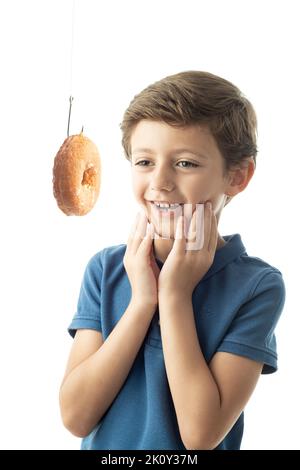 Un enfant regarde un gâteau de Savoie accroché à un crochet. Image montrant le concept de la dépendance au sucre et aux aliments sucrés. Fond blanc et sp Banque D'Images
