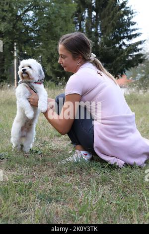 Une femelle tenant son mignon chien bichon Havanais avec des arbres en arrière-plan Banque D'Images
