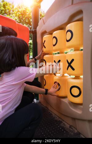 Enfant fille jouant au jeu TIC-tac-TOE au terrain de jeu dans le parc. Banque D'Images