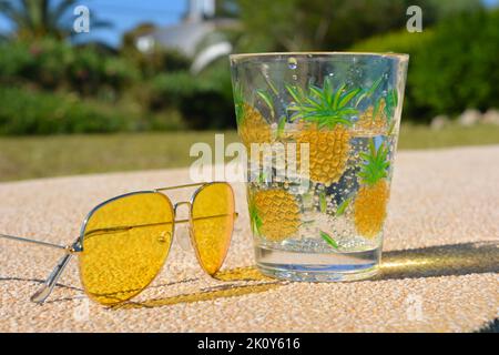 Lunettes de soleil jaunes à côté d'une boisson gazeuse froide et claire à l'extérieur Banque D'Images