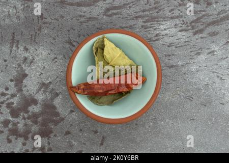 Vue en hauteur sur les feuilles de caffir et un piment rouge dans un petit bol au-dessus d'un plan d'examen gris marbré. Banque D'Images