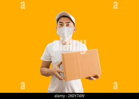 Jeune homme de livraison asiatique portant une casquette et un t-shirt blanc vierge tenant une boîte postale isolée sur fond jaune. concept de service de livraison express. Banque D'Images