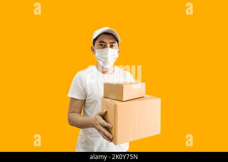 Jeune homme de livraison asiatique portant une casquette et un t-shirt blanc vierge tenant une boîte postale isolée sur fond jaune. concept de service de livraison express. Banque D'Images