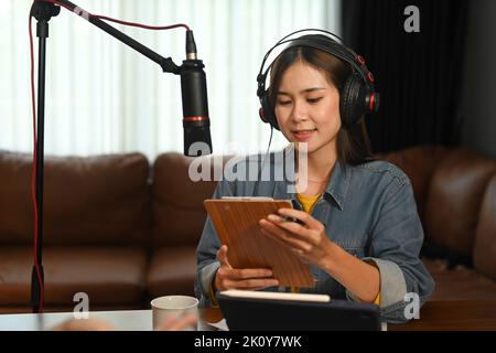 Femme asiatique podcaster portant un casque et parlant à travers le microphone pour enregistrer la conversation pour sa chaîne Banque D'Images