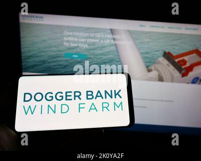 Personne tenant le téléphone cellulaire avec le logo du générateur d'énergie offshore Dogger Bank Wind Farm à l'écran en face de la page Web. Mise au point sur l'affichage du téléphone. Banque D'Images