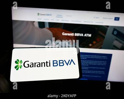 Personne tenant un téléphone portable avec le logo de la société turque de services financiers Garanti BBVA à l'écran en face de la page web. Mise au point sur l'affichage du téléphone. Banque D'Images