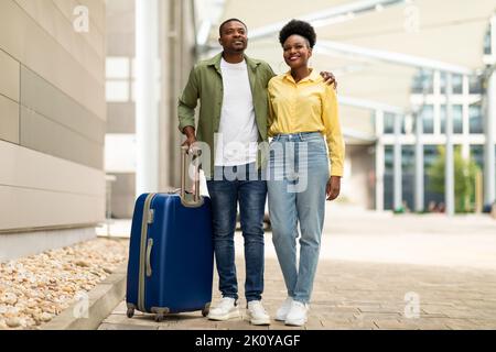 Joyeux couple noir qui se pose avec Suitcase debout à l'aéroport Banque D'Images