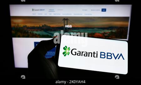 Personne tenant le téléphone portable avec le logo de la société turque de services financiers Garanti BBVA sur l'écran devant le web. Mise au point sur l'affichage du téléphone. Banque D'Images