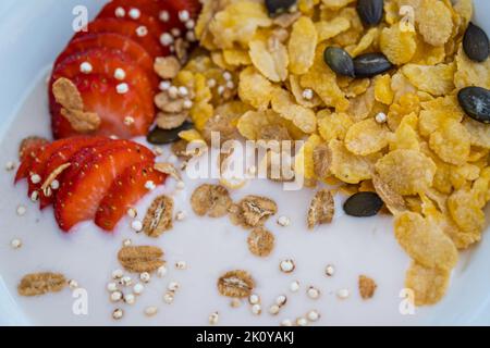 Bol à yaourt avec des fraises coupées en tranches fraîches et des flocons de maïs secs. Concept traditionnel de petit déjeuner à base de céréales. Concept de saine alimentation. Alimentation et santé Banque D'Images