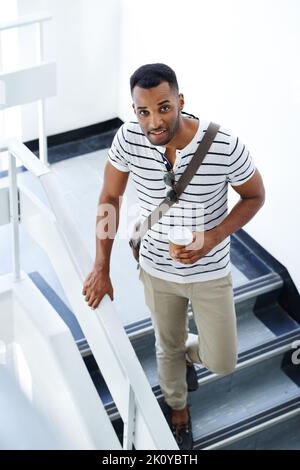 Peut-être l'ascenseur aurait-il été plus rapide... Un jeune homme d'affaires élégant et décontracté qui descendait dans les escaliers tout en tenant son mobile et son café. Banque D'Images