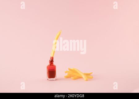 Pomme de terre frite trempée dans un vernis à ongles rouge avec une pile de frites sur le côté sur fond rose. Concept minimal. Banque D'Images