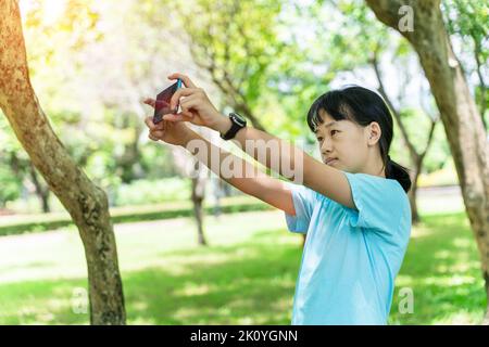 portrait d'une jeune fille asiatique à l'aide d'un smartphone mobile dans le parc, par une chaude journée de printemps. Banque D'Images