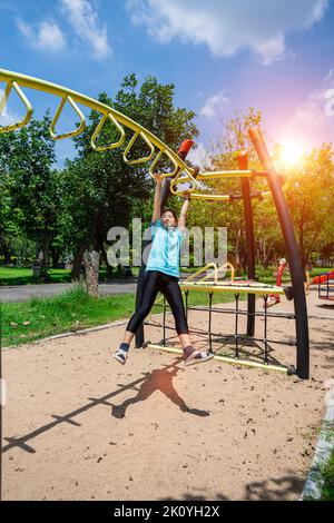 Une petite fille adorable qui pendait sur des barres de singes à l'aire de jeux du parc à l'extérieur. Petite fille mignonne s'amuser dans le jardin d'été. Banque D'Images