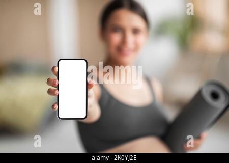 Publicité mobile. Femme enceinte tenant un smartphone avec un écran vierge et un tapis de yoga Banque D'Images