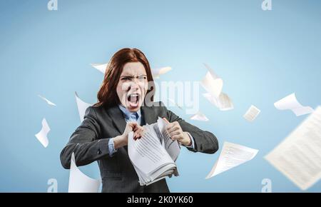 Jeune femme stressée déchirant des documents avec une expression faciale frustrée. Banque D'Images