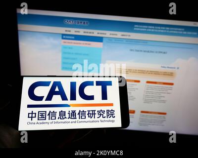 Personne tenant l'ohone mobile avec le logo de l'institut chinois de recherche sur les communications CAICT à l'écran en face de la page Web. Mise au point sur l'affichage du téléphone. Banque D'Images