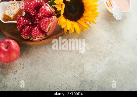 Roch Hachana. Grenade mûre, pomme, miel et tournesol, fleurs jaunes sur fond gris rustique. Composition avec symboles automne juif Rosh a Banque D'Images