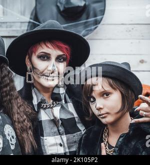 Famille, mère et fille effrayantes célébrant halloween. Terrifiante tête de mort noire demi-visage maquillage et sorcière costumes, images stylées.Horror, amusement à enfantr Banque D'Images