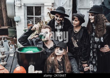 Famille effrayante, mère, père, filles célébrant halloween. Chou-fleur de potion.terrifiant crâne noir maquillage demi-visage, costumes de sorcière, image élégante Banque D'Images