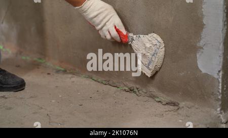 Le maître sur une spatule métallique applique la solution sur le mur pour le nivellement. Le maître applique la solution avec une spatule. Banque D'Images
